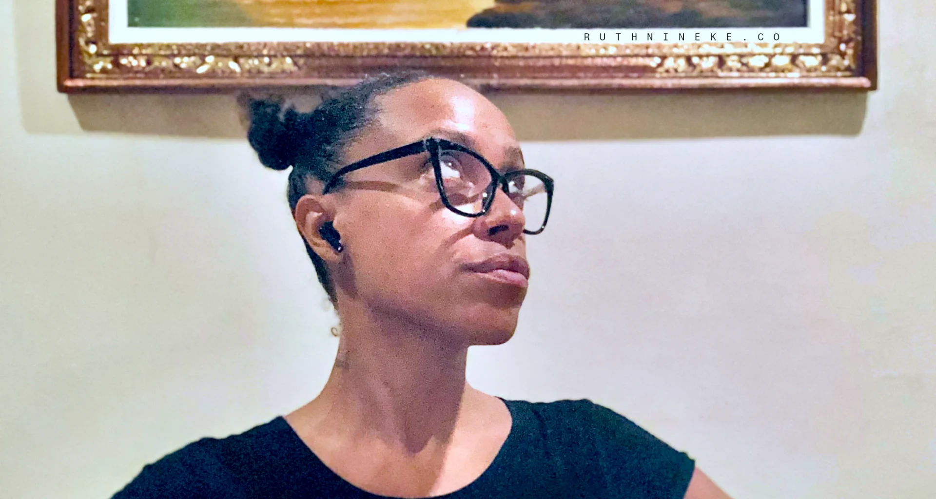 Creative professional Ruth Nineke wears black rimmed glasses and a black shirt as she stares expectantly upward.
