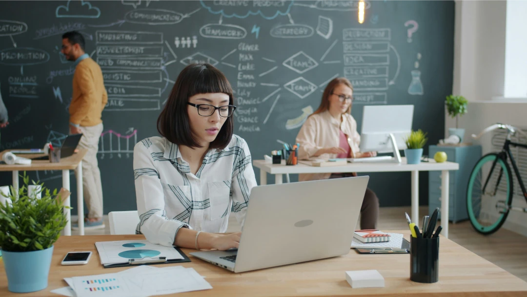 people in a room using computers and there is a chalkboard behind them